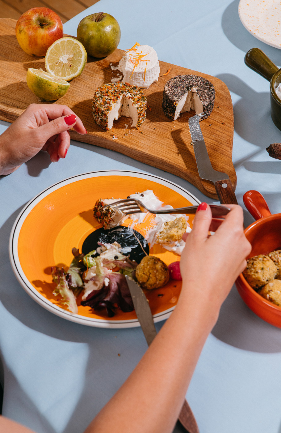 Hellblauer Tisch mit Orangen Tellern weibliche Hände Essen frische Zutaten wie Gemüse und veganen Käse