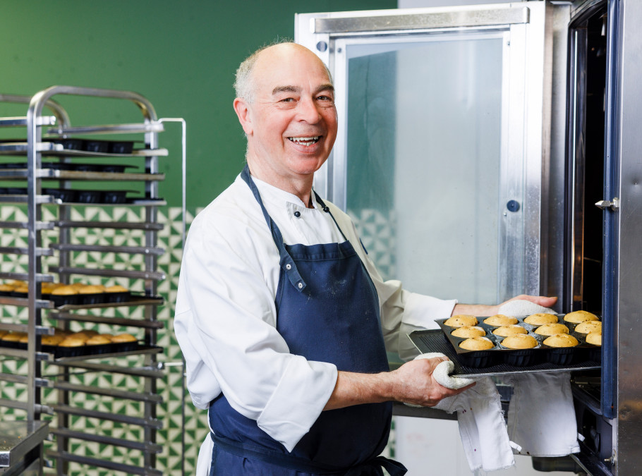 Konditor mit Schürze zieht lachend ein Blech hausgemachte Muffins aus dem Ofen