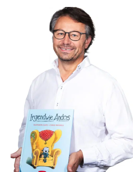 Mann mit einem Kinderbuch lächelt in die Kamera