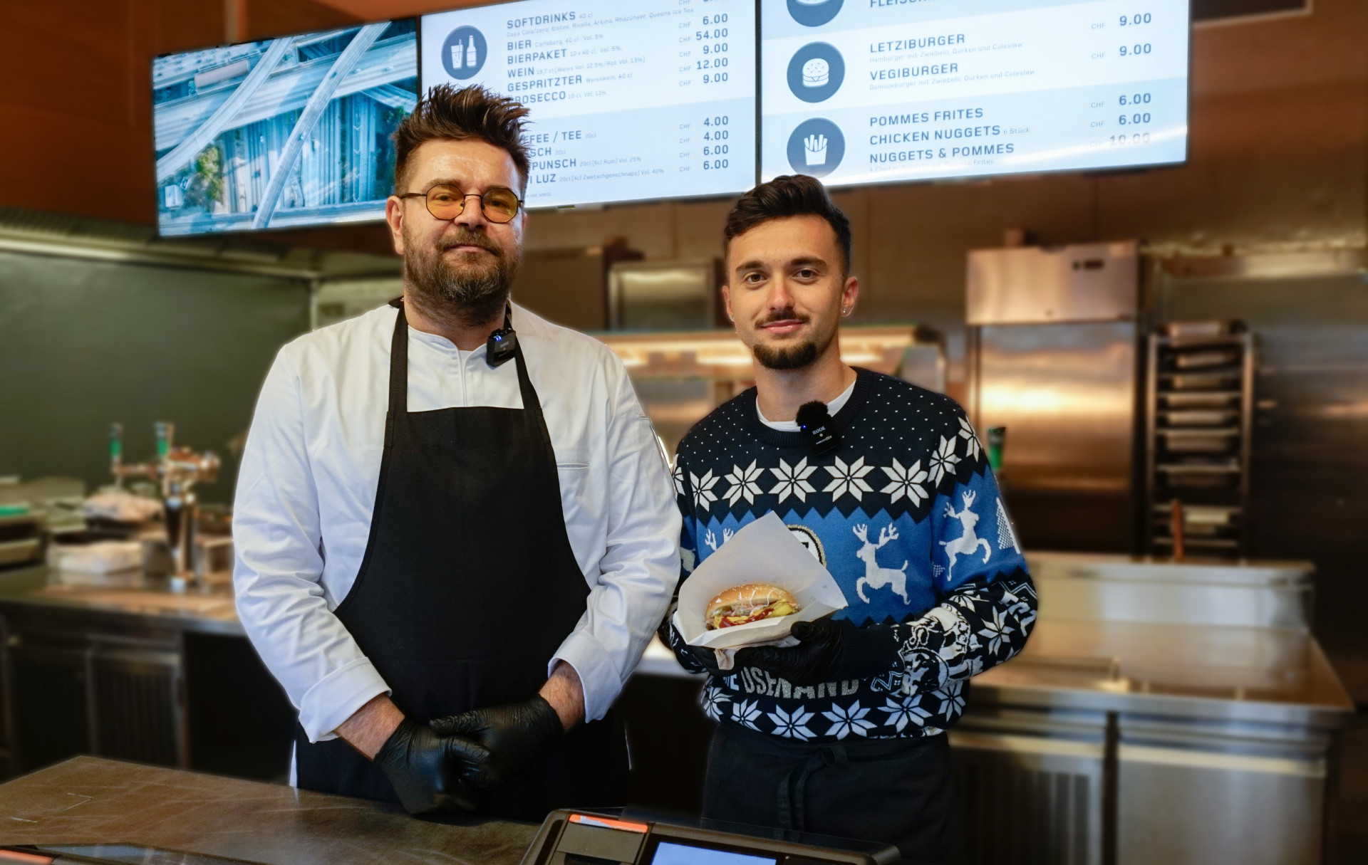 Zwei Männer stehen in einer Essensausgabe mit digitalen Screens im Hintergrund