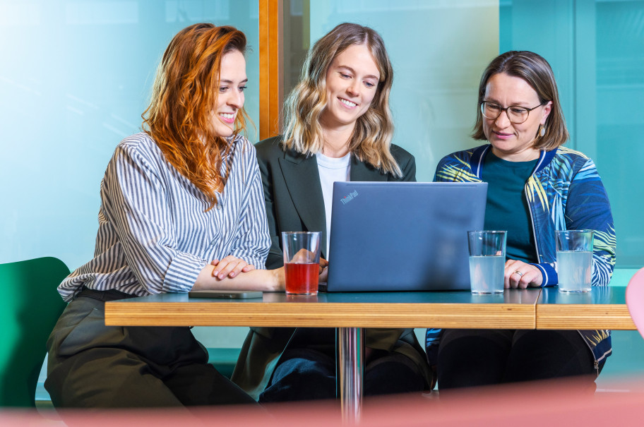 Drei Frauen sitzen an einem Laptop und besprechen eine Arbeit
