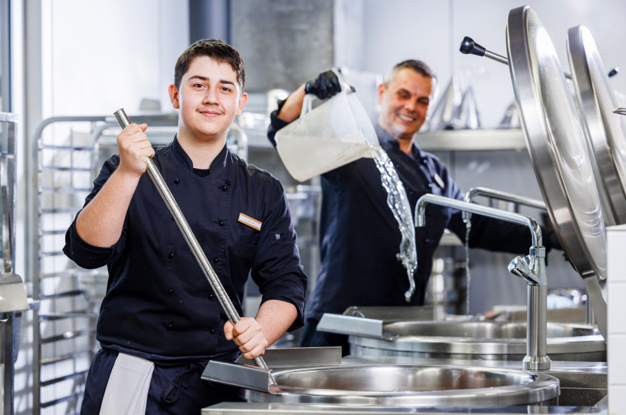 Junger Mann rührt in einem Gastronomiekochtopf