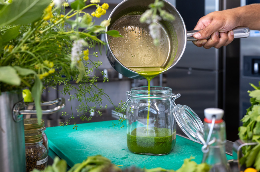 Pfanne mit Kräutersud wird in eine Glasflasche geschüttet