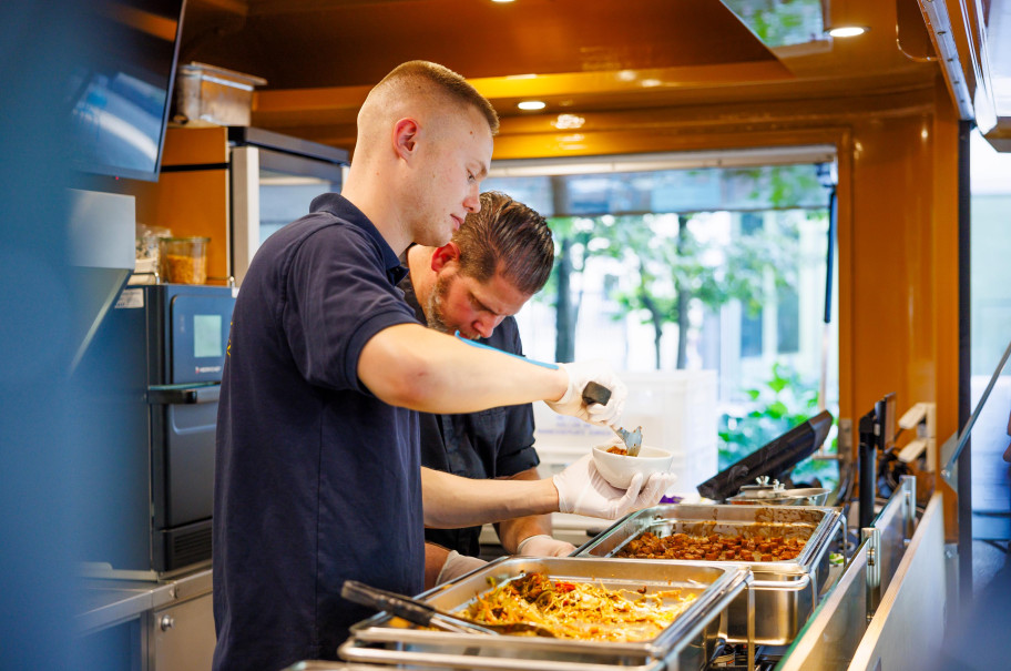 Zwei Männer schöpfen in einem Foodtruck Essen