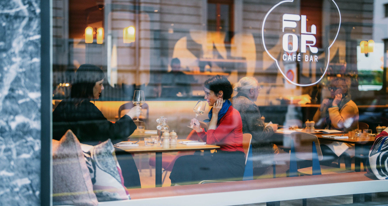 Glasfront eines Restaurants mit Logo, durch das Glas sind die Gäste im Restaurant zu sehen
