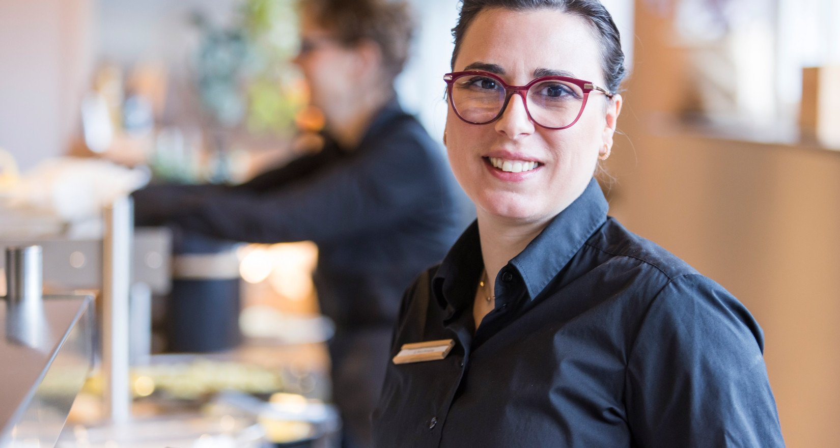 Frau lächelt in die Kamera, im Hintergrund ist ein Restaurant zu sehen