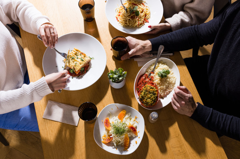 Tisch aus der Vogelperspektive mit veganen Gerichten und mehreren Menschen beim Essen