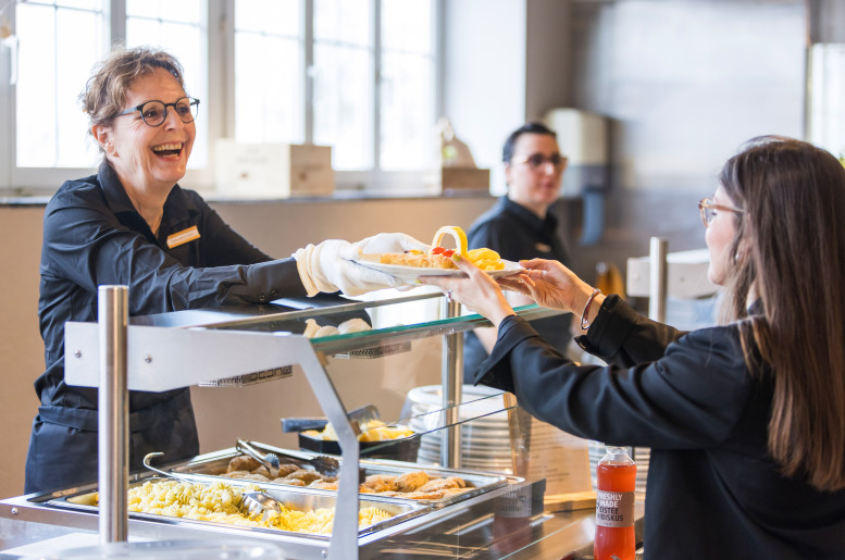 Mitarbeitende übergibt einen Teller mit Essen an einen Gast