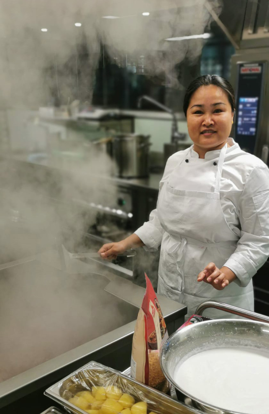 Junge Frau steht in einer Gastronomieküche und blickt in die Kamera