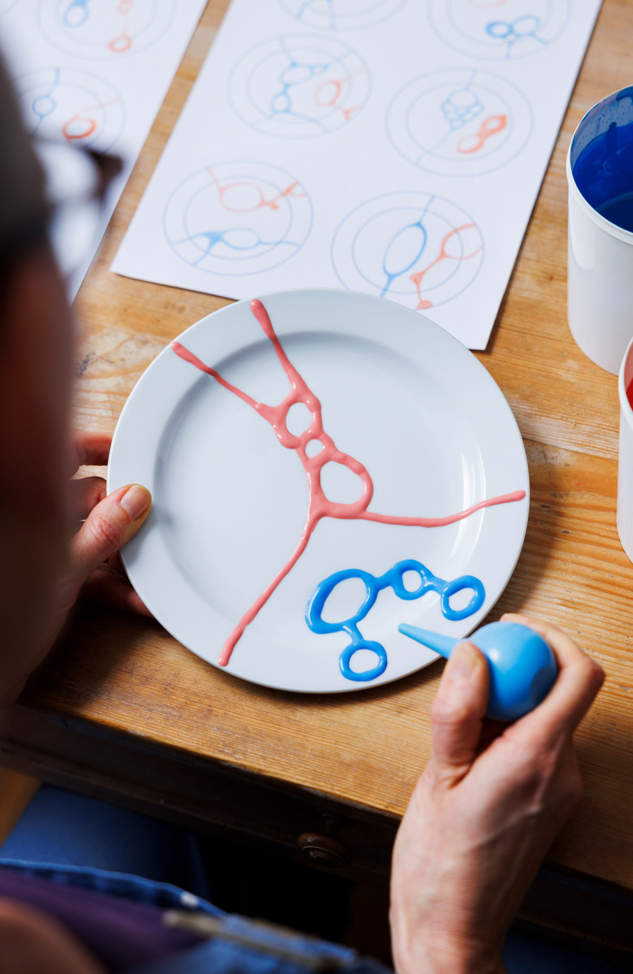 Keramikkünstlerin verziert einen Teller nach einer vor ihr liegenden Skizze