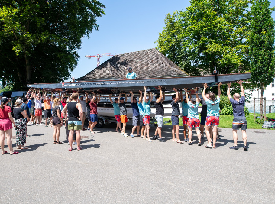 Menschen tragen in einer Gruppe ein Drachenboot zum See