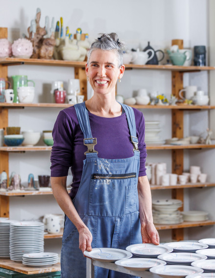 Frau in Latzhosen steht vor einem Tisch mit Tellern in einem Keramikatelier