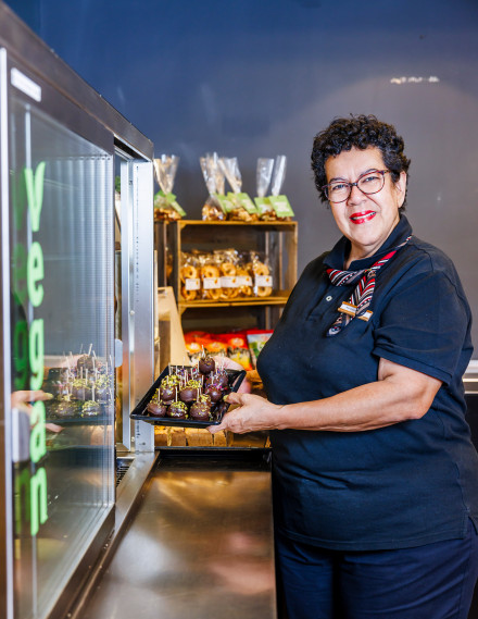 Frau nimmt ein Tableau mit Cakepops aus einer Kühlvitrine