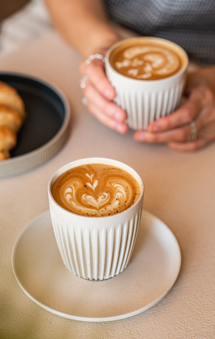 Kaffee auf einem Tisch und eine Kaffee-Tasse in der Hand