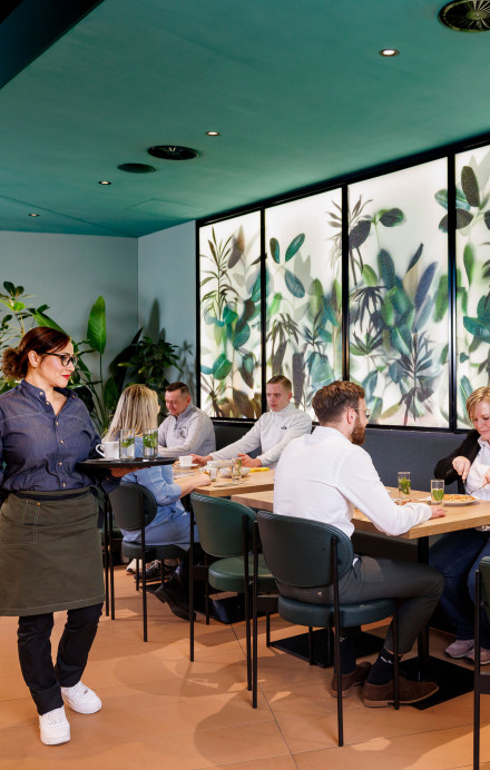 Restaurant mit Gästen, die an verschiedenen Tischen sitzen, eine Restaurantfachfrau bedient